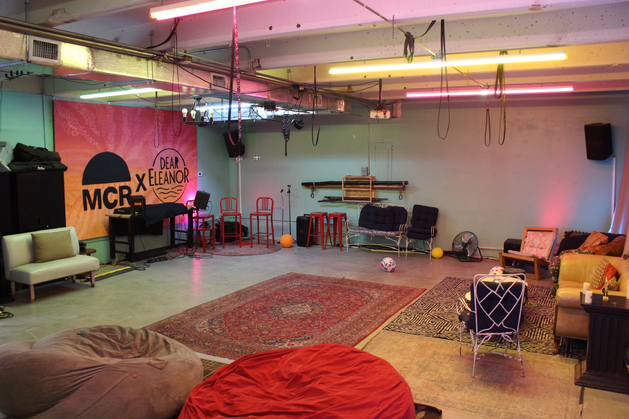 A wide view of Dear Eleanor with rugs, seating, performance space, and warm lights