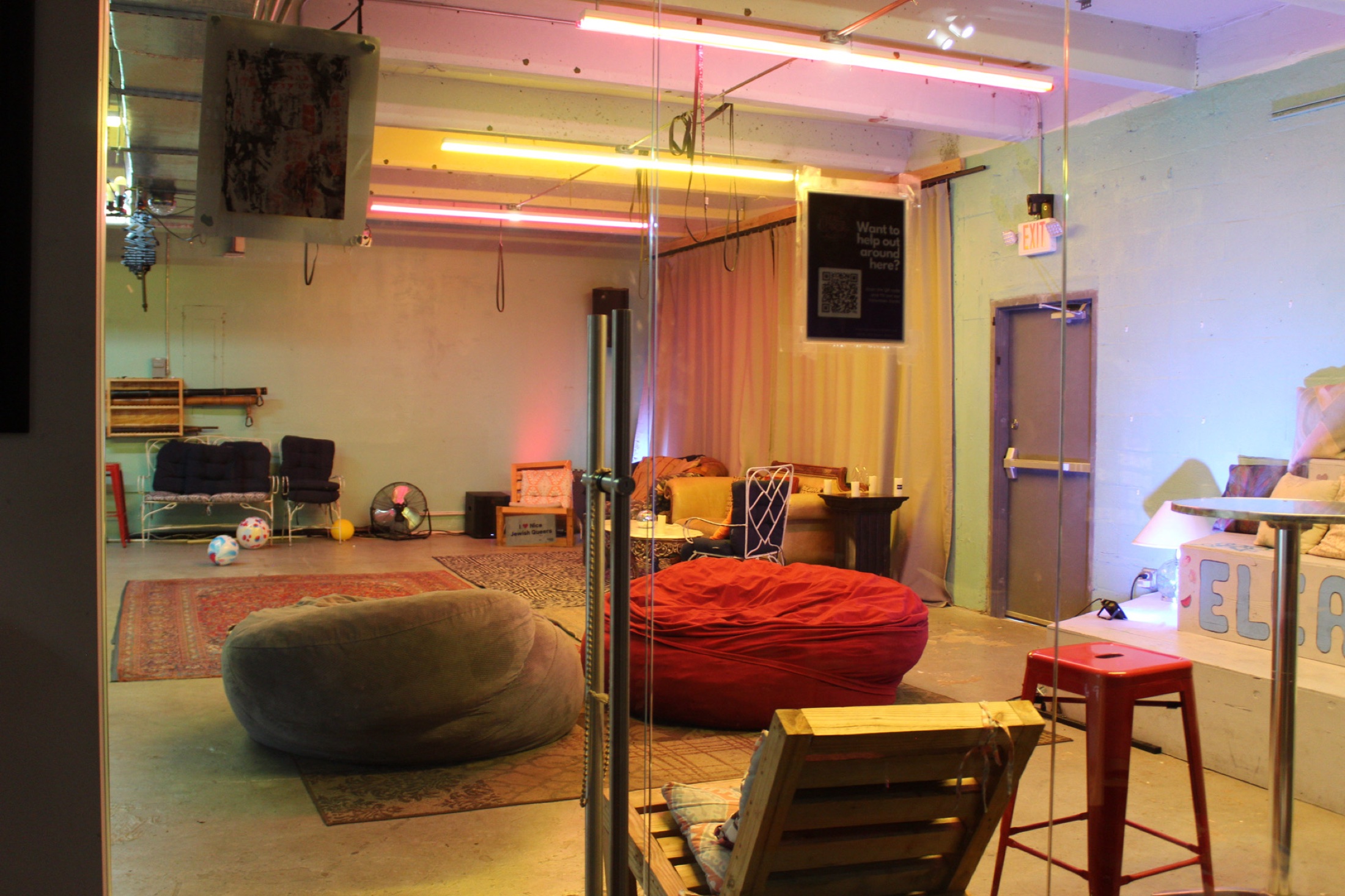 A view into the Dear Eleanor room through glass with cozy seating and warm lights